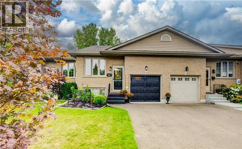 Brick exterior with a peaked roofline, attached garage, paved driveway, and manicured landscaping - 16 Steed Court, Brantford, ON 
