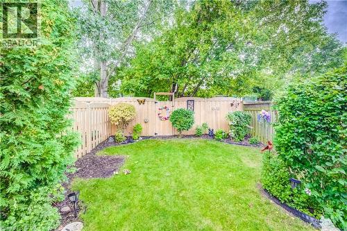 Fenced backyard featuring a manicured lawn, established landscaping, and mature perimeter trees - 16 Steed Court, Brantford, ON 