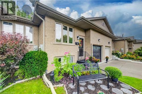 Brick exterior with light-colored window frames, an attached garage, and a paved driveway - 16 Steed Court, Brantford, ON 