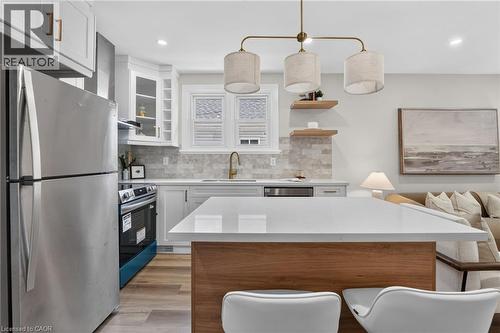 Contemporary kitchen featuring light wood-finish flooring, white cabinetry, a large center island with a white countertop, and a tiled backsplash - 43 E Brucedale Avenue E, Hamilton, ON 
