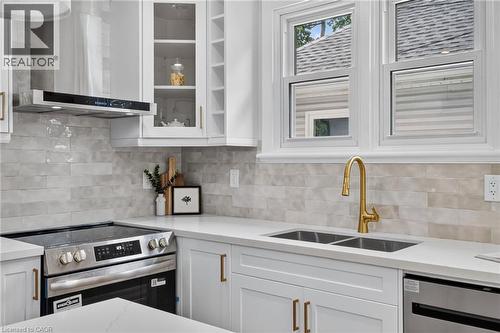 Modern kitchen featuring white cabinetry with brass-finish hardware, stainless steel appliances, and a double-basin sink with a brass-finish faucet - 43 E Brucedale Avenue E, Hamilton, ON 