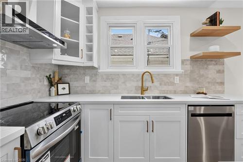 White shaker cabinetry with gold-tone hardware, stainless steel appliances, light-toned stone-finish backsplash, white quartz countertops, and a gold-tone faucet - 43 E Brucedale Avenue E, Hamilton, ON 