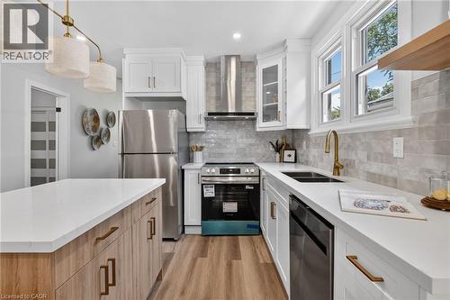 Modern kitchen with white cabinetry, stainless steel appliances, wood-finish flooring, and a stone-look backsplash - 43 E Brucedale Avenue E, Hamilton, ON 