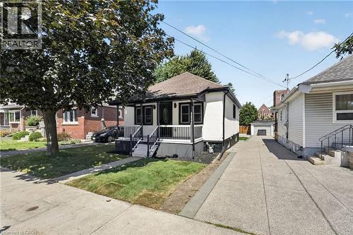 White exterior with black trim, covered front porch, concrete driveway, and detached garage - 43 E Brucedale Avenue E, Hamilton, ON 