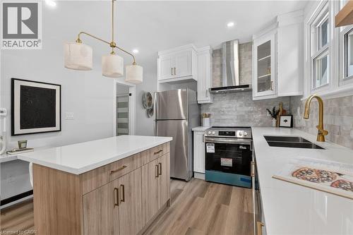 Kitchen featuring white cabinetry, light wood-finish flooring, stainless steel appliances, a center island with a light-toned countertop, and a brass-finish faucet - 43 E Brucedale Avenue E, Hamilton, ON 
