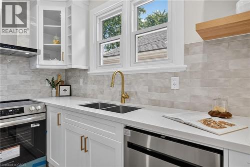 White cabinetry with gold-tone hardware, stainless steel appliances, dual basin sink with a gold-tone faucet, and light-toned tile backsplash - 43 E Brucedale Avenue E, Hamilton, ON 