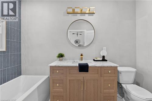 Oak-finish vanity with a white countertop, circular mirror, and gold-finish vanity light - 43 E Brucedale Avenue E, Hamilton, ON 