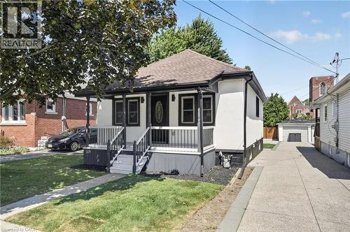 Front porch with dark railing, white exterior, and a detached garage with a long driveway - 43 E Brucedale Avenue E, Hamilton, ON 