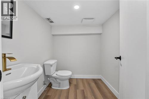 Wood-finish flooring, modern pedestal sink, gold-finish faucet, and recessed lighting - 43 E Brucedale Avenue E, Hamilton, ON 