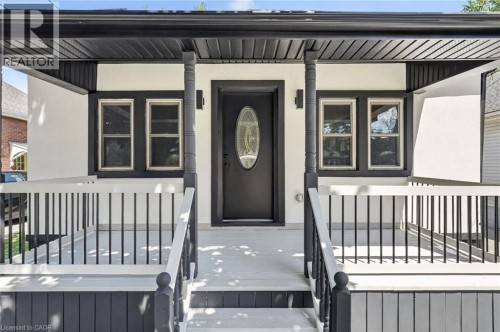 Covered front porch with black railings, decorative porch columns, and a black front door with oval-shaped glass insert - 43 Brucedale Avenue E, Hamilton, ON 
