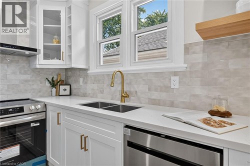 White cabinetry with gold-tone hardware, stainless steel appliances, dual basin sink with a gold-tone faucet, and light-toned tile backsplash - 43 Brucedale Avenue E, Hamilton, ON 