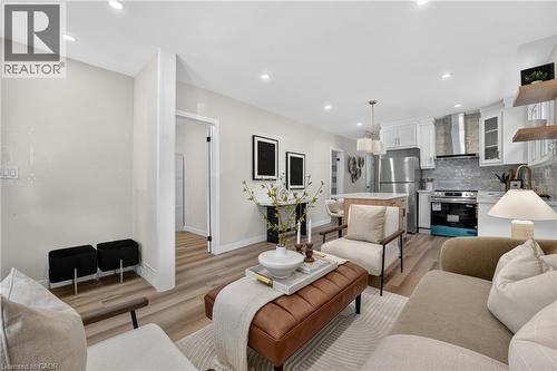 Open-concept living space featuring wood-finish flooring, recessed lighting, and a kitchen with white cabinetry, stainless steel appliances, and a tiled backsplash - 43 E Brucedale Avenue E, Hamilton, ON 
