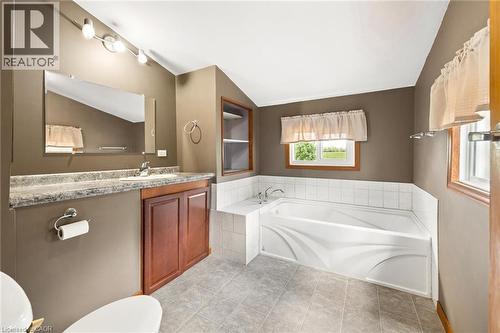 Corner soaking tub, single vanity with wood-finish cabinetry, countertop, tile flooring, and built-in wall shelving - 5480 Line 42 Line, Mitchell, ON 
