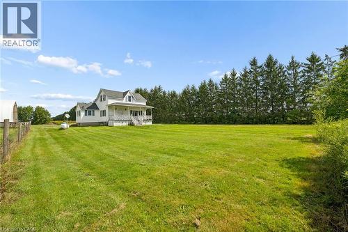 Expansive green lawn, white residential structure, covered porch, partial perimeter fencing, and mature evergreen trees - 5480 Line 42 Line, Mitchell, ON 