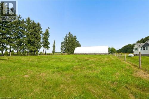 Expansive green space with mature evergreen trees, a large white agricultural structure, and a partial exterior of a residence - 5480 Line 42 Line, Mitchell, ON 