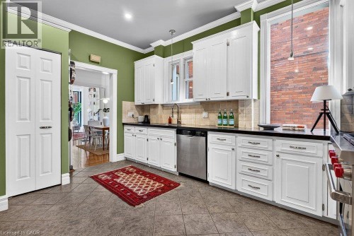Kitchen featuring white cabinetry, dark countertops, a stainless steel dishwasher, tile flooring, and a tiled backsplash - 16 Bruce Street, Hamilton, ON 