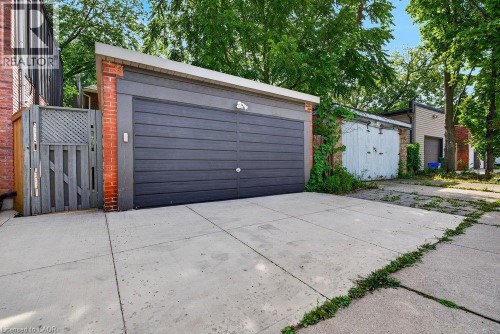 Concrete driveway leading to a detached garage with a dark gray paneled door and brick accents - 16 Bruce Street, Hamilton, ON 