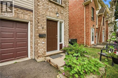 Brick exterior with a brown panel door, single-car garage, and established front landscaping - 384 Limeridge Road E Unit# 16, Hamilton, ON 