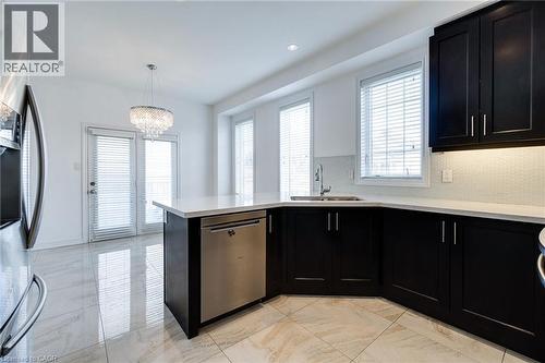 Modern kitchen featuring dark cabinetry, light countertops, a stainless steel dishwasher, and a tile backsplash - 2 Hawstone Road, Vellore, ON 