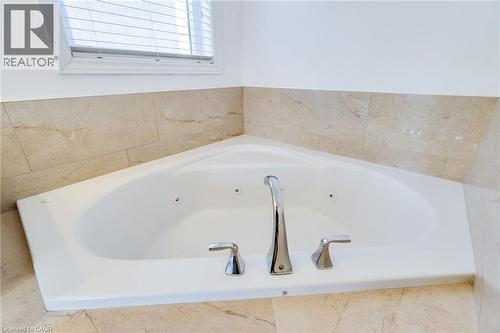 White corner soaking tub with chrome fixtures, integrated jets, and surrounding natural stone tile - 2 Hawstone Road, Vellore, ON 