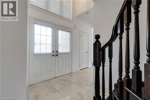 Double entry doors with glass panels, light-toned tiled flooring, dark wood-finish staircase with turned balusters, and a transom window above the entry - 2 Hawstone Road, Vellore, ON 