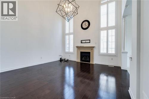 High ceilings with a geometric chandelier, wood-finish flooring, a fireplace with a stone mantel, and tall windows with plantation shutters - 2 Hawstone Road, Vellore, ON 