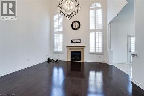 High ceilings featuring a geometric chandelier, fireplace with a stone mantel, wood-finish flooring, and arched windows with plantation shutters - 2 Hawstone Road, Vellore, ON 