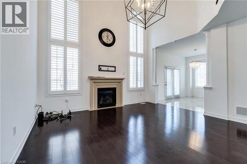 Two-story windows with plantation shutters, dark wood-finish flooring, a fireplace with a stone mantel, a geometric light fixture, and architectural columns - 2 Hawstone Road, Vellore, ON 