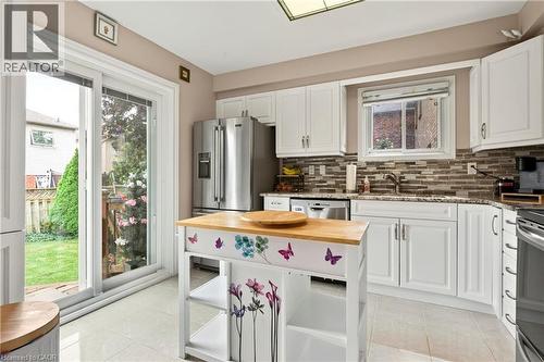 White cabinetry with silver-tone hardware, stainless steel refrigerator, tile backsplash, and light-toned countertops - 31 Grindstone Way, Hamilton, ON 