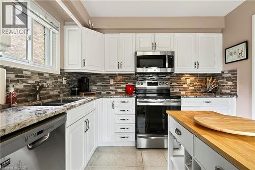 White shaker-style cabinetry, stainless steel appliances, a mosaic tile backsplash, a double basin sink, and wood-finish flooring - 31 Grindstone Way, Hamilton, ON 