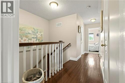 Wood-finish flooring throughout, with a white baluster staircase and wood-finish handrail - 31 Grindstone Way, Hamilton, ON 