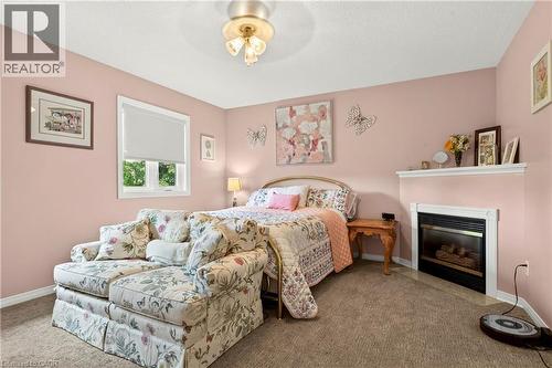 Recessed fireplace with white mantel, wall-mounted light fixture, light-colored carpeting, and a window with a roller shade - 31 Grindstone Way, Hamilton, ON 