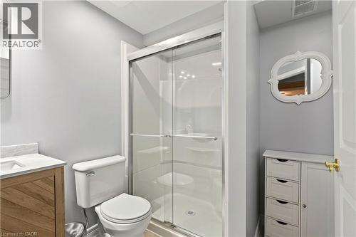 Glass-enclosed shower, white toilet, wood-finish vanity with countertop, white storage cabinet, and wall-mounted mirror - 31 Grindstone Way, Hamilton, ON 