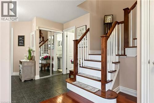 Hardwood staircase with white risers and balusters, dark wood newel posts and handrails, dark tile flooring, and mirrored closet doors - 31 Grindstone Way, Hamilton, ON 