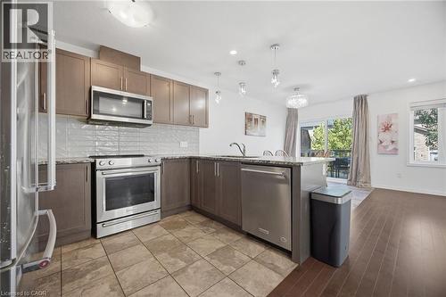 Modern kitchen featuring stainless steel appliances, wood-finish cabinetry, a tile backsplash, and a breakfast bar with pendant lighting - 135 Hardcastle Drive Unit# 85, Cambridge, ON 