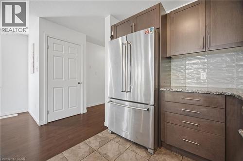 Stainless steel refrigerator, wood-finish cabinetry, stone countertop, tile backsplash, and wood-finish flooring - 135 Hardcastle Drive Unit# 85, Cambridge, ON 