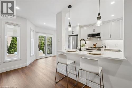White kitchen cabinetry with stainless steel appliances, a white tile backsplash, and a breakfast bar with pendant lighting - 2294 Seton Crescent, Burlington, ON 