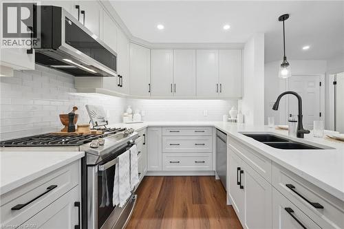 U-shaped kitchen featuring white cabinetry, stainless steel appliances, solid surface countertops, and wood-finish flooring - 2294 Seton Crescent, Burlington, ON 