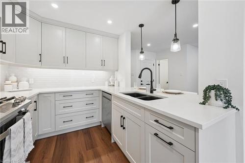 Contemporary kitchen featuring white cabinetry with black hardware, white subway tile backsplash, white countertops, wood-finish flooring, and a black double basin sink with a gooseneck faucet - 2294 Seton Crescent, Burlington, ON 
