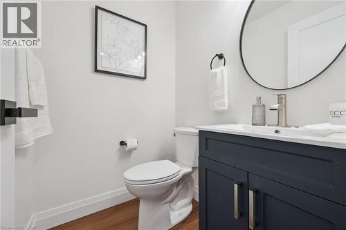 Powder room featuring a dark blue vanity with a white countertop and rectangular sink, a circular mirror, and wood-finish flooring - 2294 Seton Crescent, Burlington, ON 
