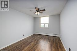 Wood-finish flooring with light gray walls, a window with a roller shade, and an overhead ceiling fan with integrated lighting - 