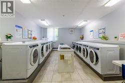 On-site laundry facility featuring multiple front-loading washers and dryers, utility sink, and tiled flooring - 