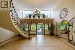 Two-story foyer with a curved staircase featuring wrought iron railing, tile flooring, exposed brick accents, and a multi-tiered chandelier - 