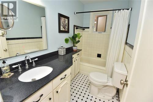 Bathroom featuring a dark speckled countertop, white oval sink with chrome faucet, light blue wall paint, and black and white hexagonal floor tiles - 936 Boothman Avenue, Burlington, ON 