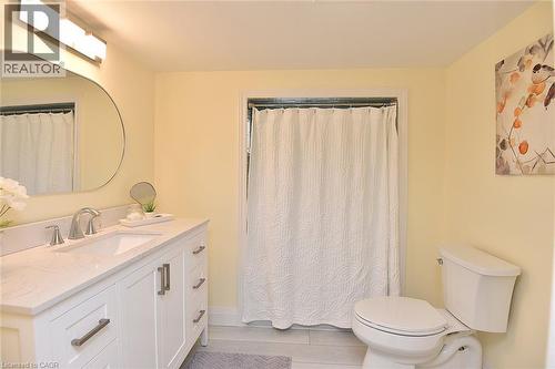 White vanity with an integrated sink and brushed nickel hardware, paired with a coordinating round mirror and a three-light vanity fixture - 936 Boothman Avenue, Burlington, ON 