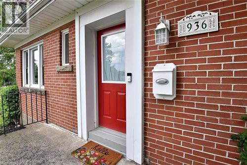 Brick exterior featuring a bright red entry door with sidelight, white window trim, and a concrete entry porch - 936 Boothman Avenue, Burlington, ON 