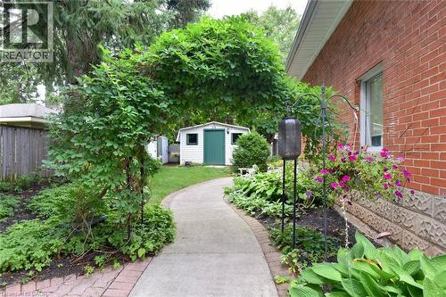 Arched garden trellis, concrete pathway, red brick exterior, landscaped garden beds, and a white storage shed with a green door - 936 Boothman Avenue, Burlington, ON 