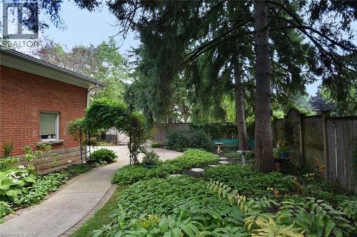 Brick exterior with a concrete pathway, an arched arbor, mature trees, and a wood fence - 936 Boothman Avenue, Burlington, ON 