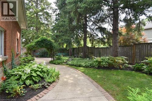 Manicured landscaping with mature trees, a concrete pathway bordered by brick, and a decorative garden arch - 936 Boothman Avenue, Burlington, ON 