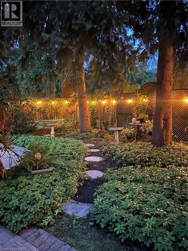 Landscaped garden featuring mature trees, string lighting, a stone pathway, and lush ground cover - 936 Boothman Avenue, Burlington, ON 